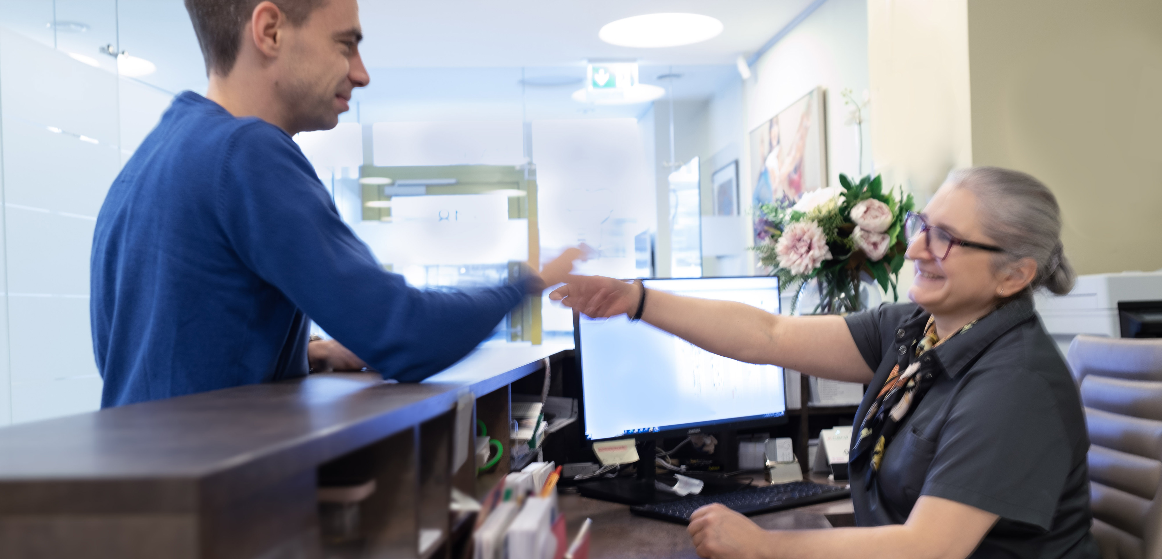Empfangsbereich Zahnarztpraxis. Patient reicht Mitarbeiterin seine E-card.