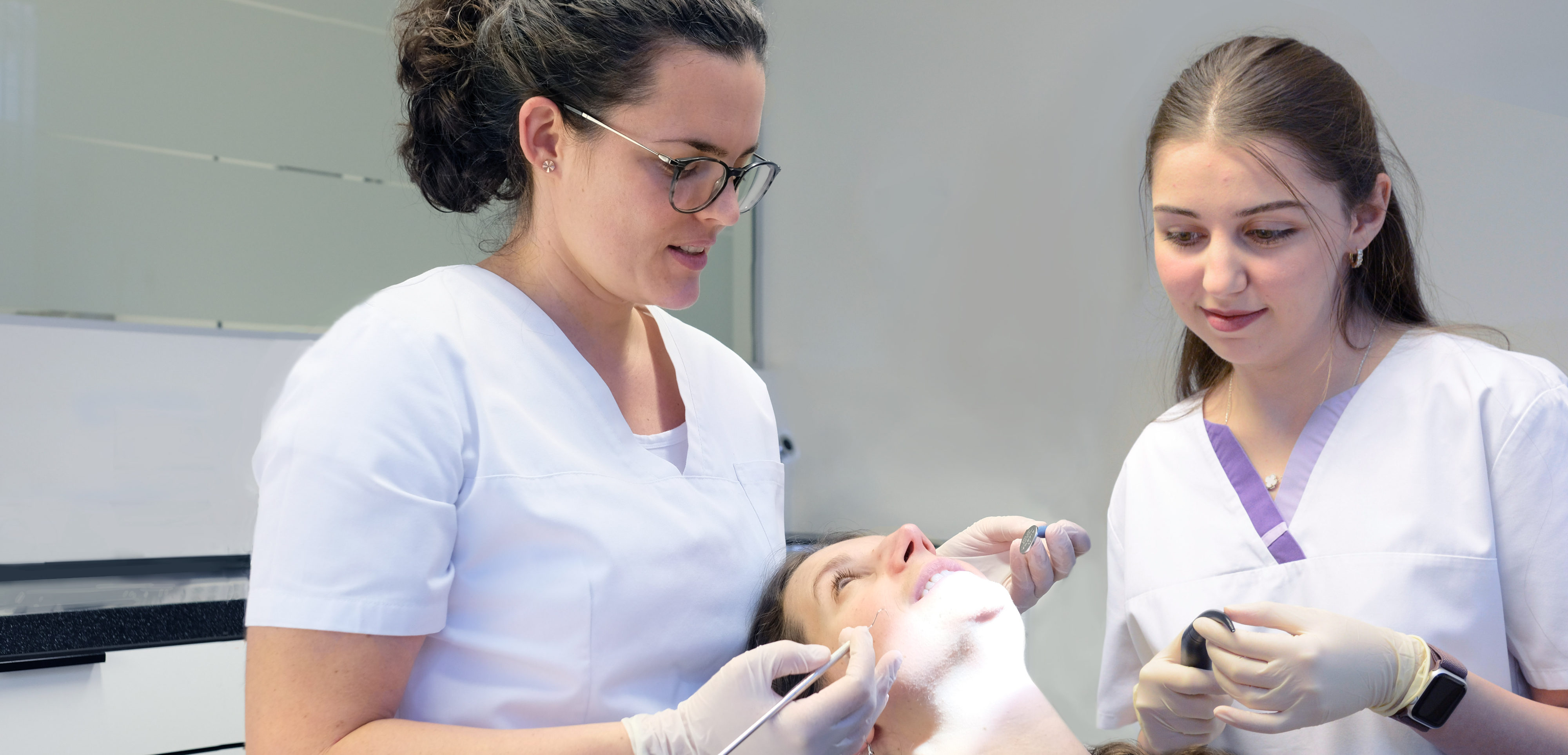Zahnärztin und Assistentin behandeln Patientin in Praxisraum.