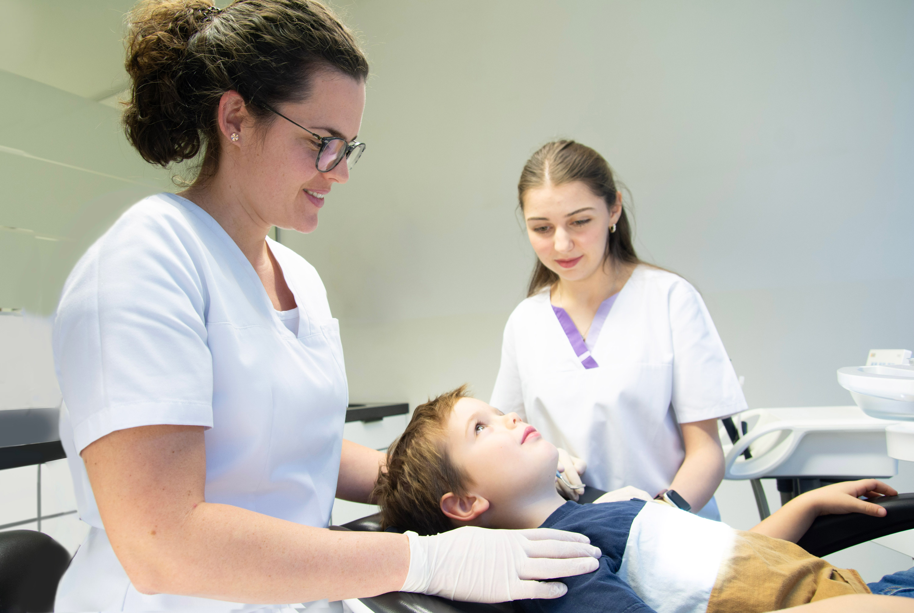 Zahnärztin und Assistentin behandeln Kind in Praxisraum.