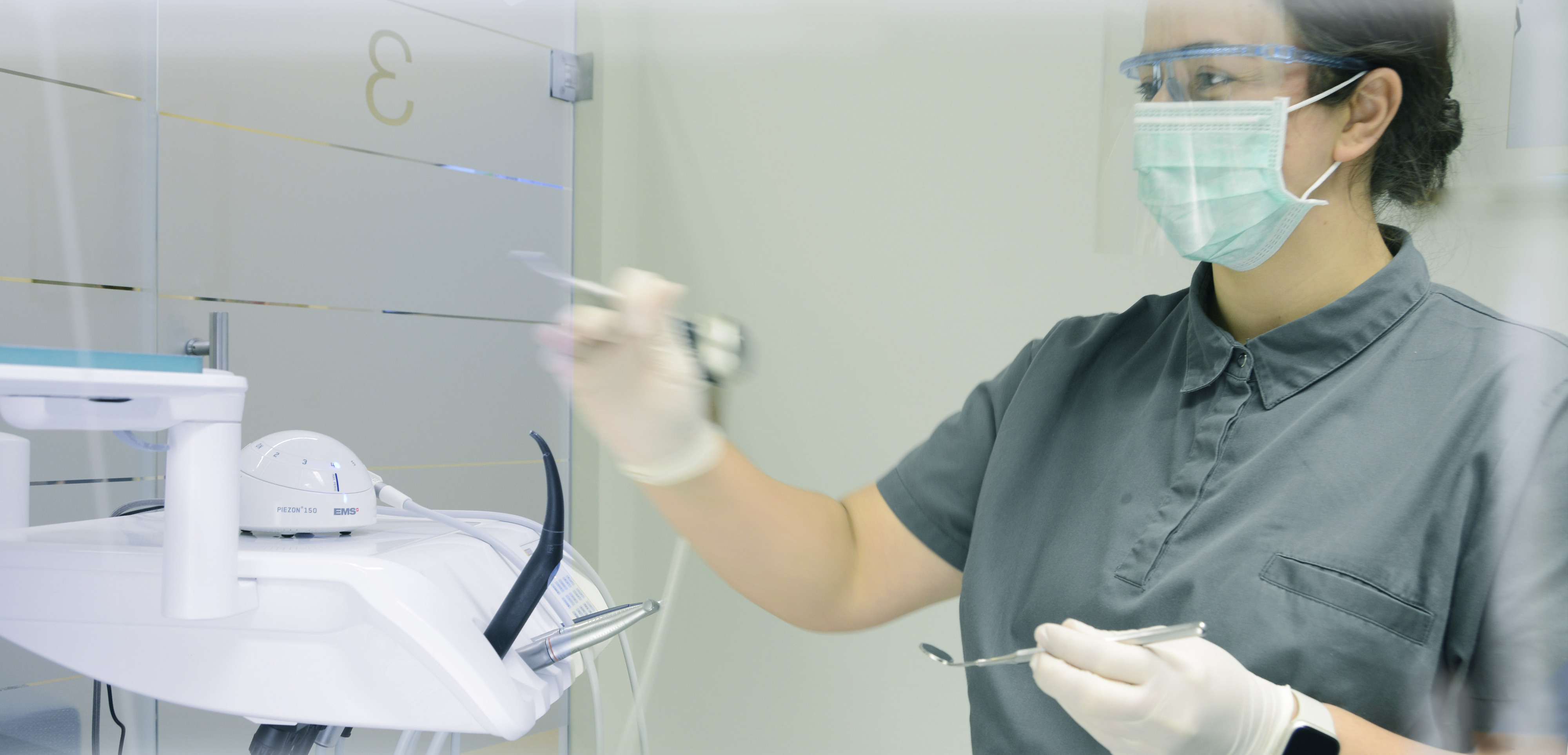 Praxisraum Zahnärztin. Zahnarztassistentin mit Mundschutz und Visier nimmt Utensilien aus Konsole.